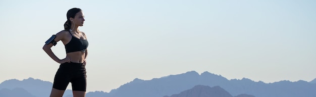 A thin athletic girl takes a break between classes on the background of mountains