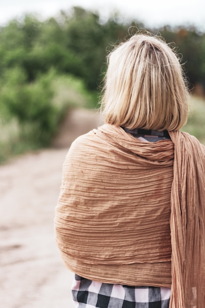 A thin blonde girl in a cape stands looks into the distance.