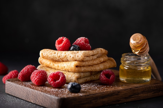 Thin homemade pancakes with berries and honey closeup