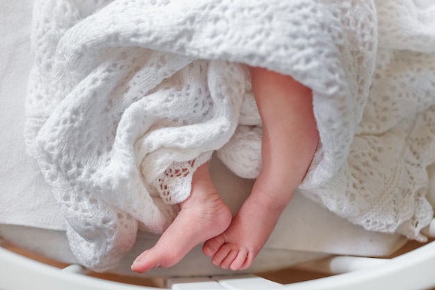 Gambe sottili del neonato in una coperta copriletto circolare intorno ai piedi del bambino un bambino coperto con una coperta a maglia di pizzo