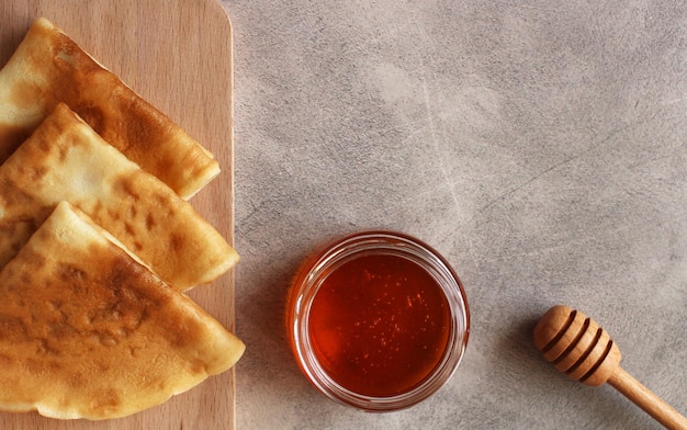 Thin pancakes folded in triangles with honey on a gray background