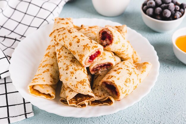 Thin pancakes rolled into rolls with berry jam on a plate on the table