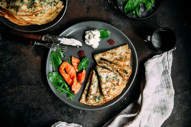 Thin pancakes with herbs, salmon and cream cheese on a plate