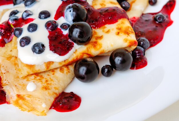 Photo thin pancakes with sweet currant and berry sauce closeup