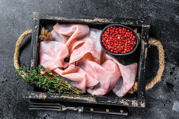 Thin sliced Smoked  pork ham in wooden tray. Black background. Top view.