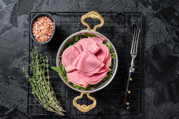 Thin slices of ham in a skillet with arugula salad Black background Top view