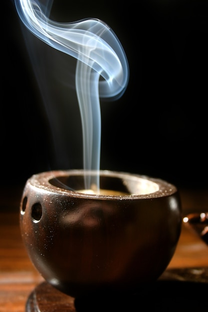 A thin trail of smoke rises from a brown cuplike incense holder