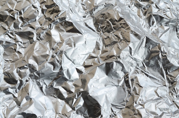 Photo thin wrinkled sheet of crushed tin aluminum silver foil background with shiny crumpled surface for texture