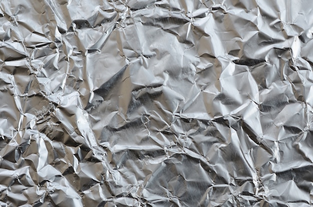 Тонкий морщинистый лист измельченной олова алюминиевой серебряной фольги фон с блестящей мятой поверхности для текстуры