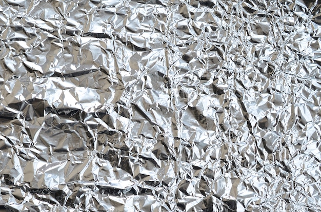 Thin wrinkled sheet of crushed tin aluminum silver foil background with shiny crumpled surface for texture