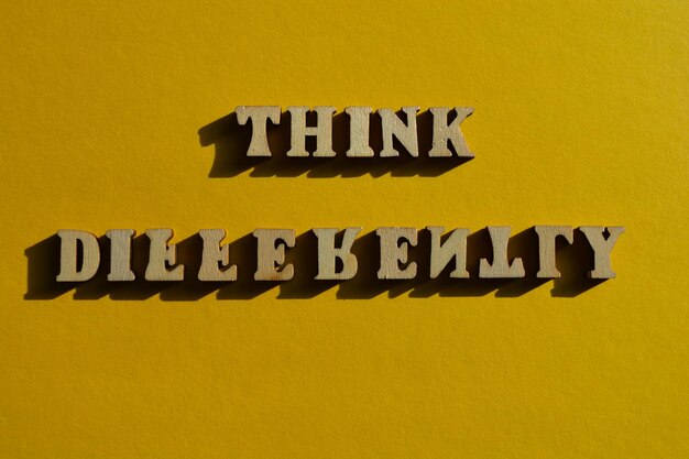 Think Differently words in wooden alphabet letters with some letters upside down isolated on yellow background