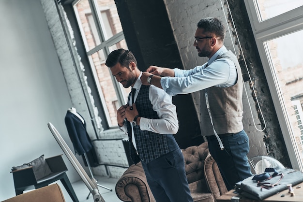 Thinking about every detail. Young fashionable designer helping his client to get dressed 