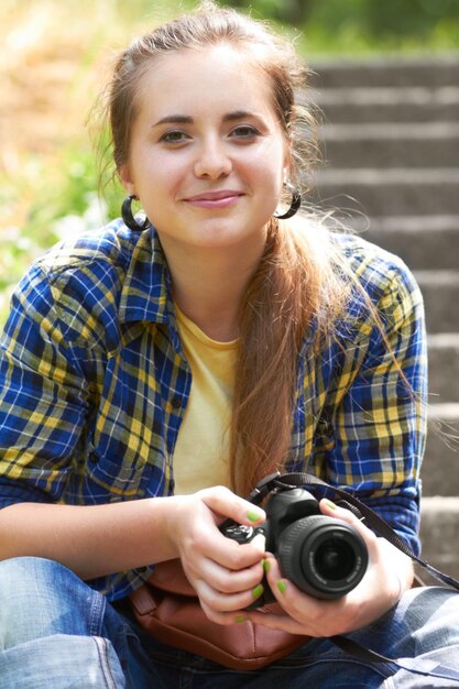 写真撮影で自分のビジネスを始めることを考えている彼女のカメラを持って彼女の庭の階段に座っているゴージャスな若い女性