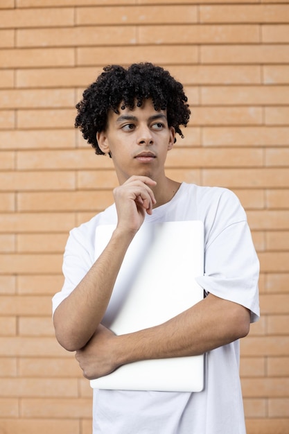 Thinking African American guy holding a closed laptop looking away and wearing tshirt