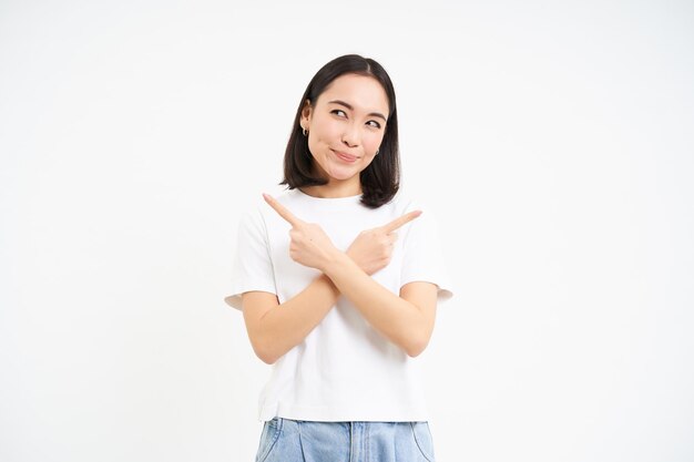 Thinking asian girl makes her decision points sideways two ways choosing stands isolated on white ba