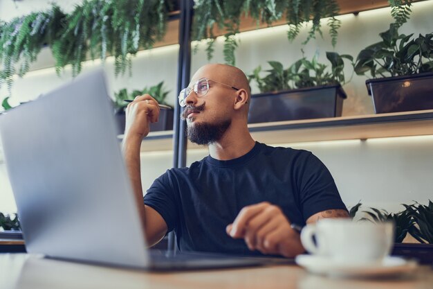 Photo thinking bald man freelancer writer or manager guy sits behind laptop looks for ideas for a project