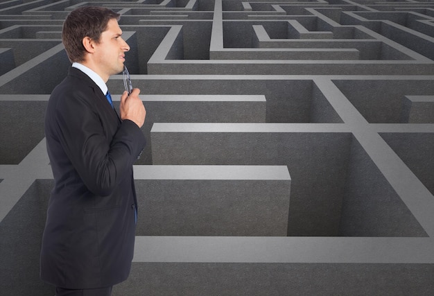 Thinking businessman holding glasses against difficult maze puzzle