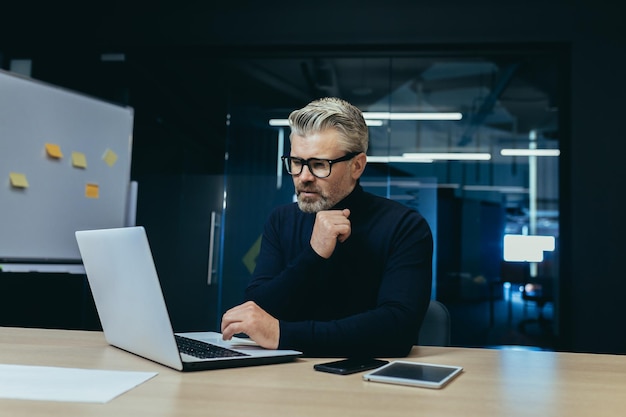 Thinking businessman inside the office with a laptop mature adult boss thinking about the decision