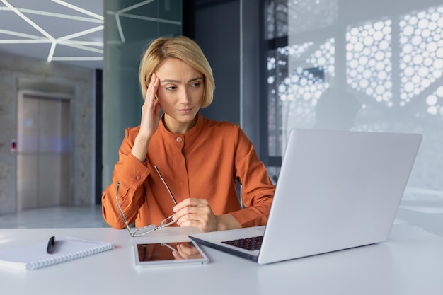 Thinking businesswoman working on laptop inside office boss working sitting at table female employee