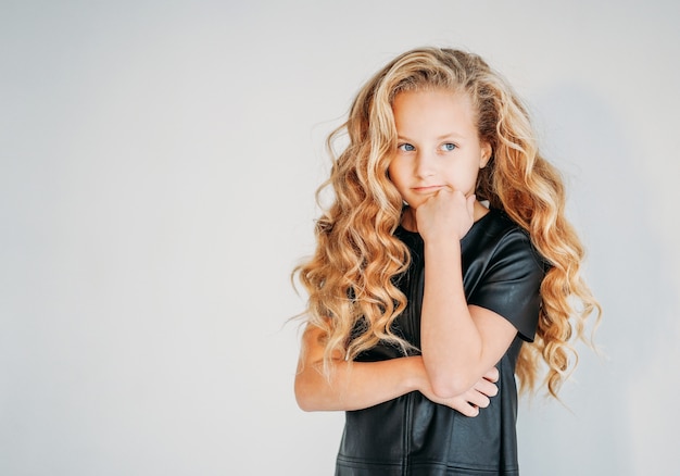 Thinking curly hair tween girl in black leather dress on white 