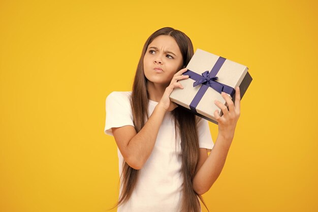 Thinking face thoughtful emotions of teenager girl Teenage child holding gift box on yellow isolated background Gift for kids birthday Christmas or New Year present box