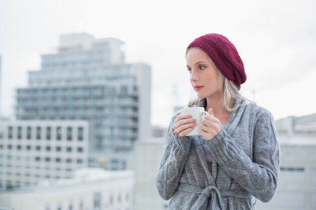 Photo thinking gorgeous blonde drinking coffee outdoors