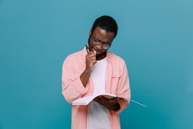 Thinking holding notebook young africanamerican guy isolated on blue background