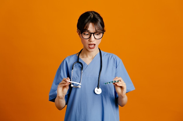 thinking holding pills young female doctor wearing uniform fith stethoscope isolated on orange background