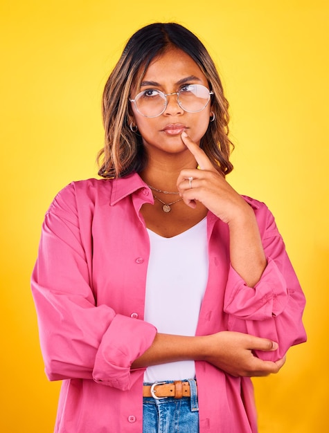 Thinking idea and face of woman on yellow background with fashion confidence or thought Inspiration style and isolated person with attitude in trendy clothes stylish outfit and glasses in studio