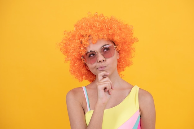 Thinking kid in curly clown wig having fun thoughtful child wear sunglasses and swimsuit