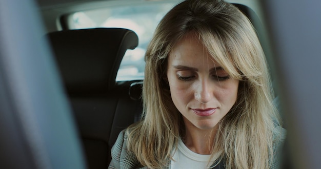 Мыслящая дама отправляет текстовое сообщение в мобильный телефон в роскошном автомобиле Портрет молодой деловой женщины, использующей мобильный телефон внутри автомобиля