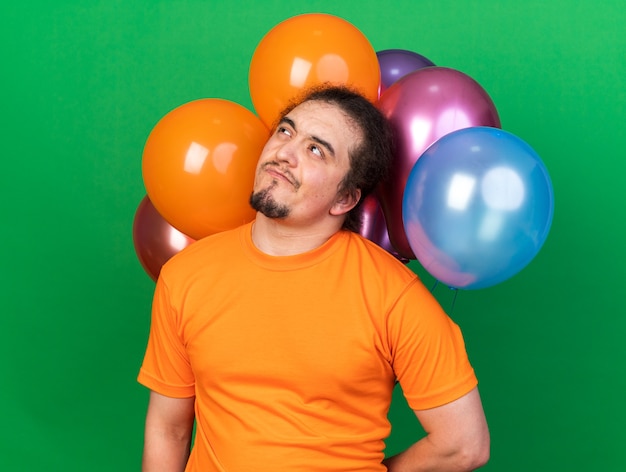 Thinking looking up young man wearing party hat standing in front balloons 