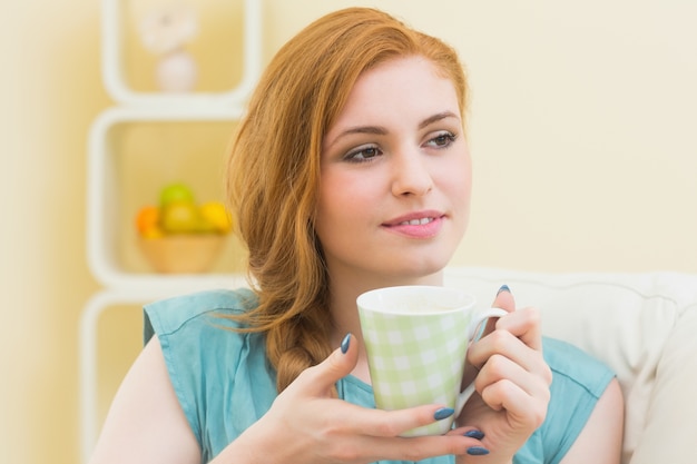 Thinking redhead sitting on the couch having coffee