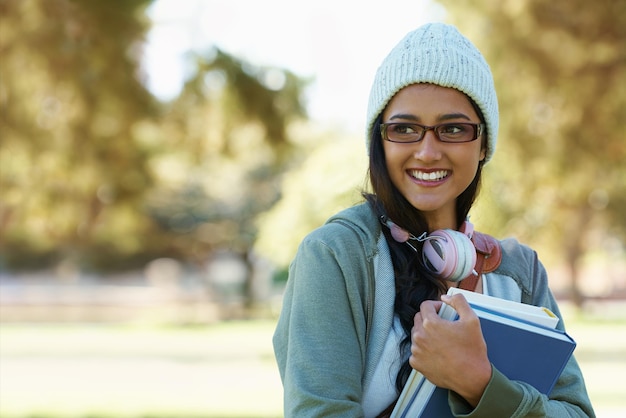 Фото Мыслящая студентка и счастливая женщина в парке с книгами для изучения обучения и чтения на открытом воздухе образовательный колледж и человек с улыбкой учебники и наушники отдыхают на природе для университета