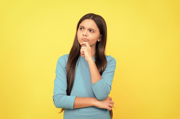 Thinking teen girl with long hair on yellow background think