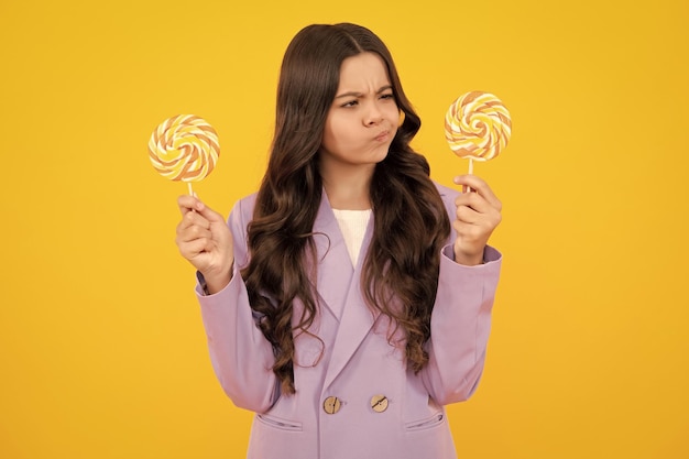 Photo thinking teenager girl thoughtful emotion teenager girl eating sugar lollypop candy and sweets for kids child eat lollipop popsicle over yellow isolated background yummy caramel candy shop