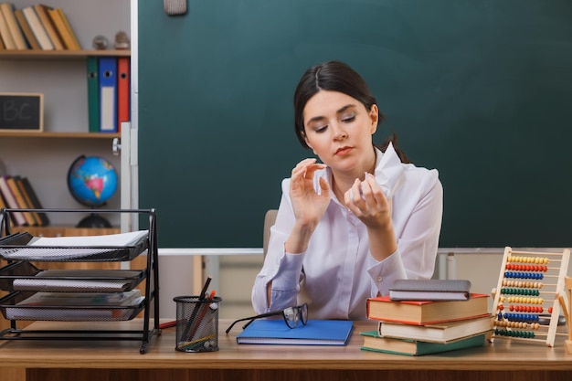 目を閉じて考える教室で学校の道具を持って机に座っている若い女性の涙の紙の先生