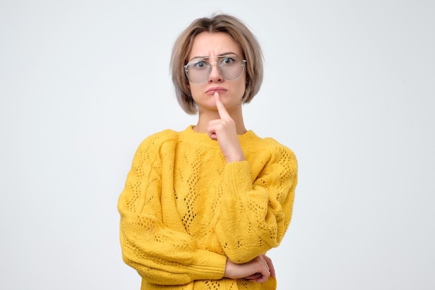 Thinking woman in yellow sweater with glasses looking at camera