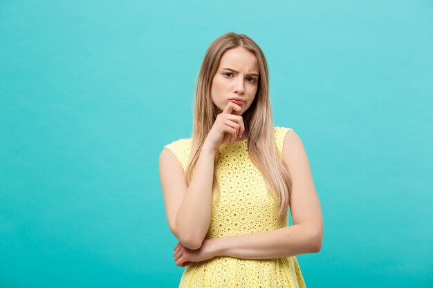 Thinking young confident woman in yellow dress looking up isolated on blue