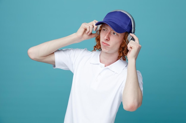 Thinking young handsome guy in cap wearing headphones isolated on blue background