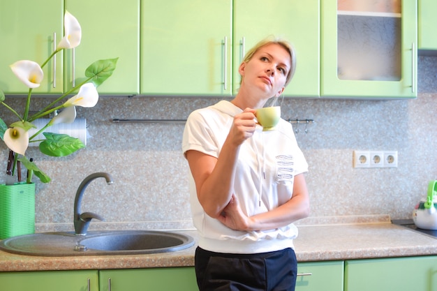 thinking young woman with a cup of drink in the kitchen thinking over an idea