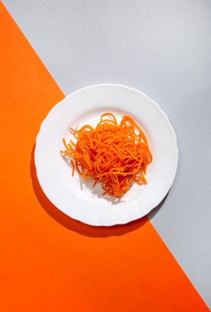 Carote affettate sottilmente su un piatto bianco su uno sfondo grigio arancio