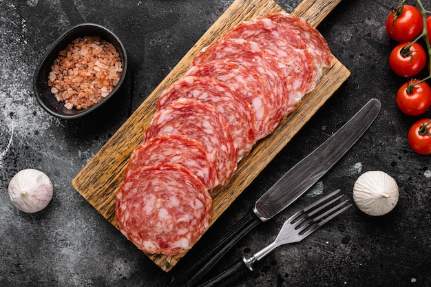Thinly Sliced Milano salami on black dark stone table background top view flat lay