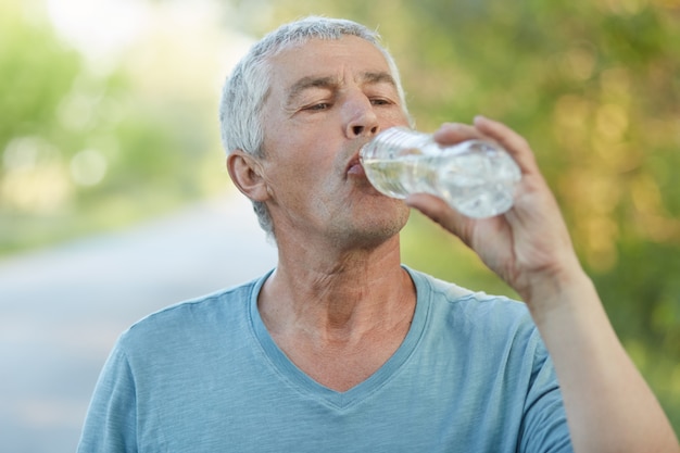 Thirsty senior male drinks water from plastic bottle