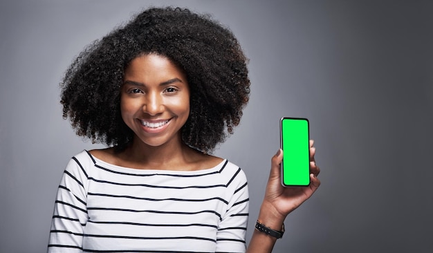 This app needs to be on your download list Studio portrait of a young woman showing a smartphone with a green screen against a gray background