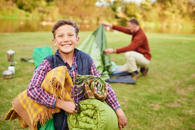 This camping trip is going to be awesome Portrait of a young boy holding camping gear with his father in the background