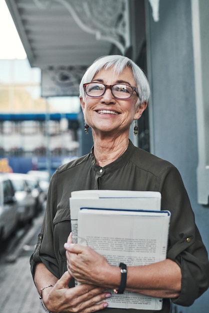 This city always reminds me of my youth Portrait of a cheerful mature businesswoman carrying books and paperwork while out in the city