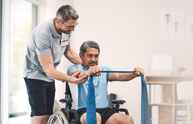 This exercise is also great for maintaining good balance Shot of a senior man in a wheelchair exercising with a resistance band along side his physiotherapist