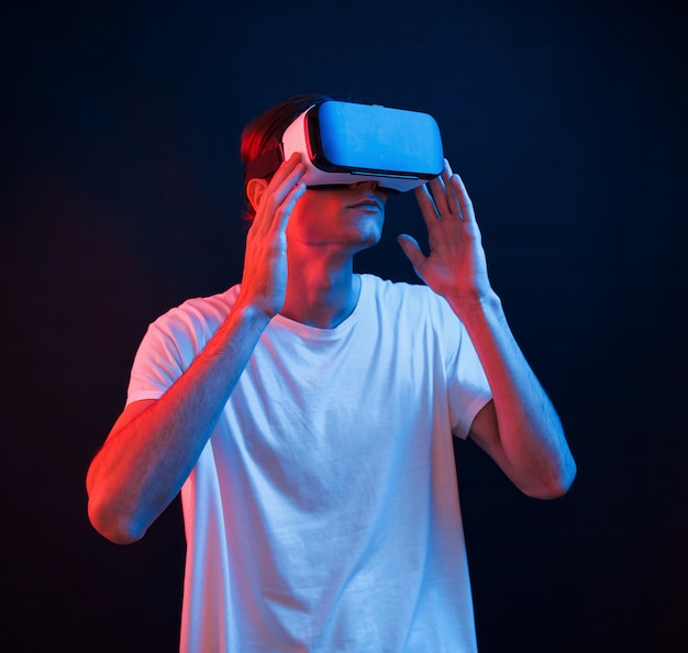 This is breathtaking. Young man using virtual reality glasses in the dark room with neon lighting