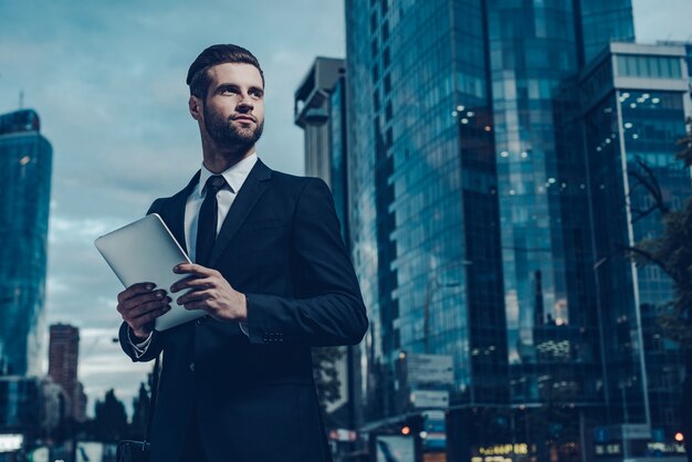 This is my city. Night time image of confident young man in full suit holding digital tablet 